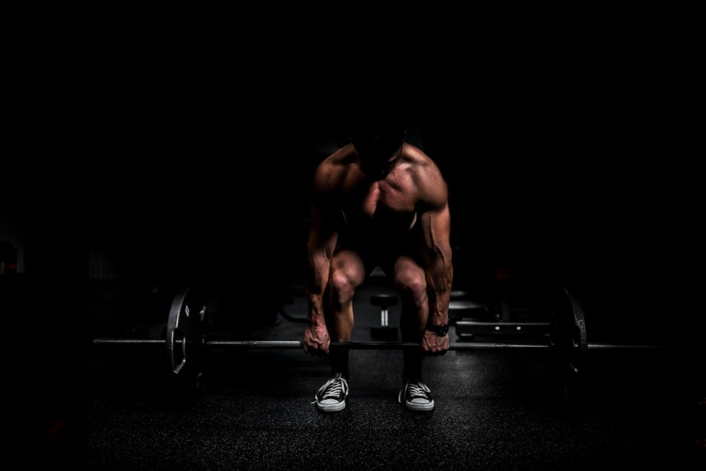 shirtless man lifting barbell in gym